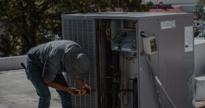 Technician using a cordless drill on a rooftop HVAC unit with its service panel open