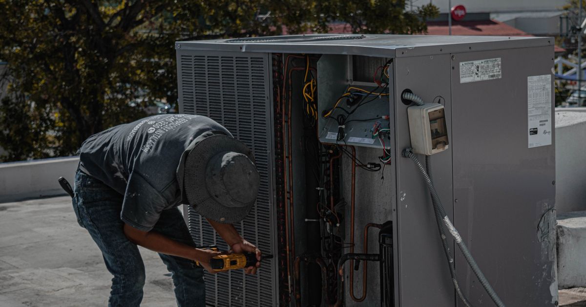 Technician using a cordless drill on a rooftop HVAC unit with its service panel open